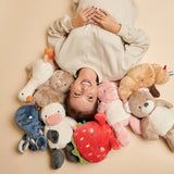 Person lying on a beige surface surrounded by colorful plush toys
