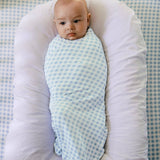 Baby wrapped in a blue and white checkered swaddle on a white pillow with a blue checkered background