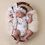 Newborn baby in a floral outfit with a bunny toy in a woven basket on a beige background