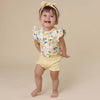 Child wearing a lemon-patterned top and yellow shorts on a beige background