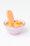 Glass bowl with colorful cereal and a wooden spoon on a white background