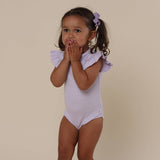 Young girl wearing a light purple onesie with ruffled sleeves on a beige background