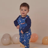 Child wearing a blue outfit with vehicle patterns, standing among balloons on a beige background