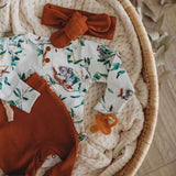 Baby outfit with floral romper, brown shorts, and bow headband on a textured surface.