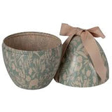 A round decorative box with a floral pattern in muted green and beige, shown open with its matching lid leaning against it and tied with a beige ribbon bow.