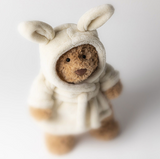 Small teddy bear wearing a white bunny costume on a light background