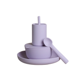 A minimalist lavender purple baby feeding set consisting of a cup with a straw, a bowl with a lid, a plate, and a spoon, all made of matte silicone on a solid white background.