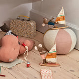 A styled collection of vintage-inspired children's toys and accessories arranged on a light wood floor against a beige wall. The set includes a large dusty pink plush hippo, a beige and pink beach ball, a floral vintage suitcase, a wooden sailboat toy, a small mouse doll, and other matching accessories.