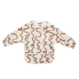 An off-white long-sleeve baby bib with a brown wavy line pattern and a front pocket, laid flat on a white background.