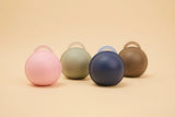 Four round, hard-shell carrying cases in pastel colors (pink, sage green, navy blue, and taupe) arranged in a row on a warm beige background.