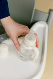 Hand holding a baby bottle over a sink