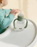 Child holding a green sippy cup with 'BIBS' branding on a light background